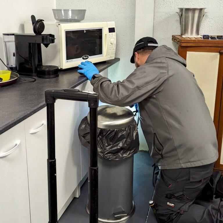 a man in a grey jacket and blue gloves working on a microwave